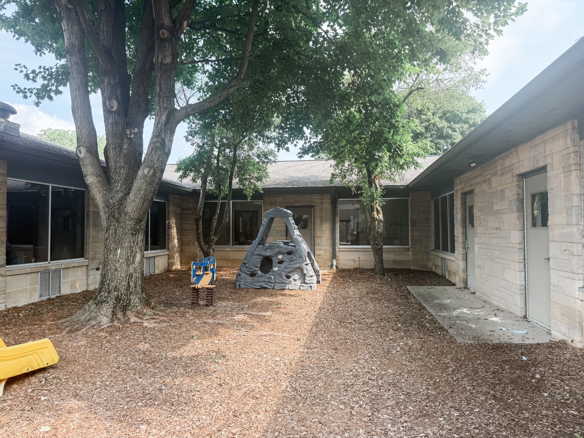 Courtyard playground shaded by a large mature tree with a rock climber