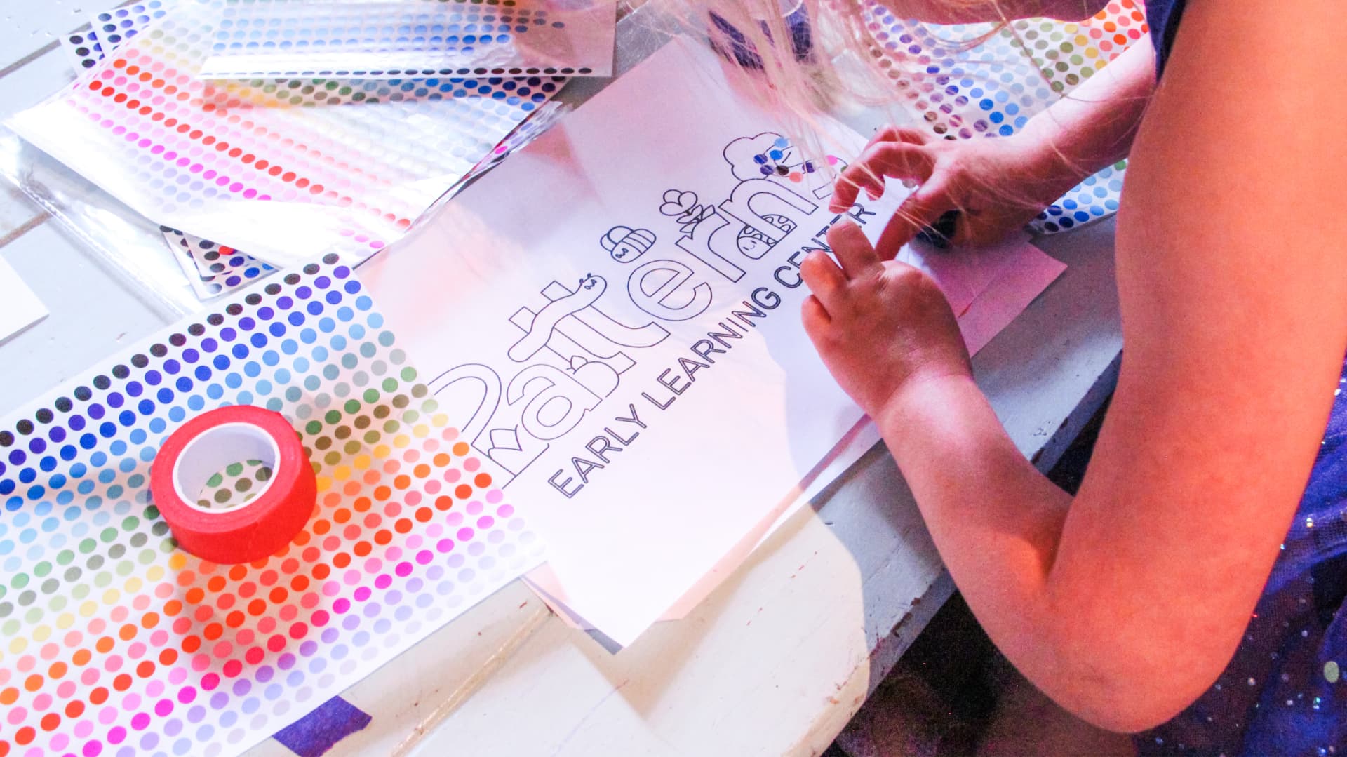 A young child decorating a Patterns coloring sheet with stickers